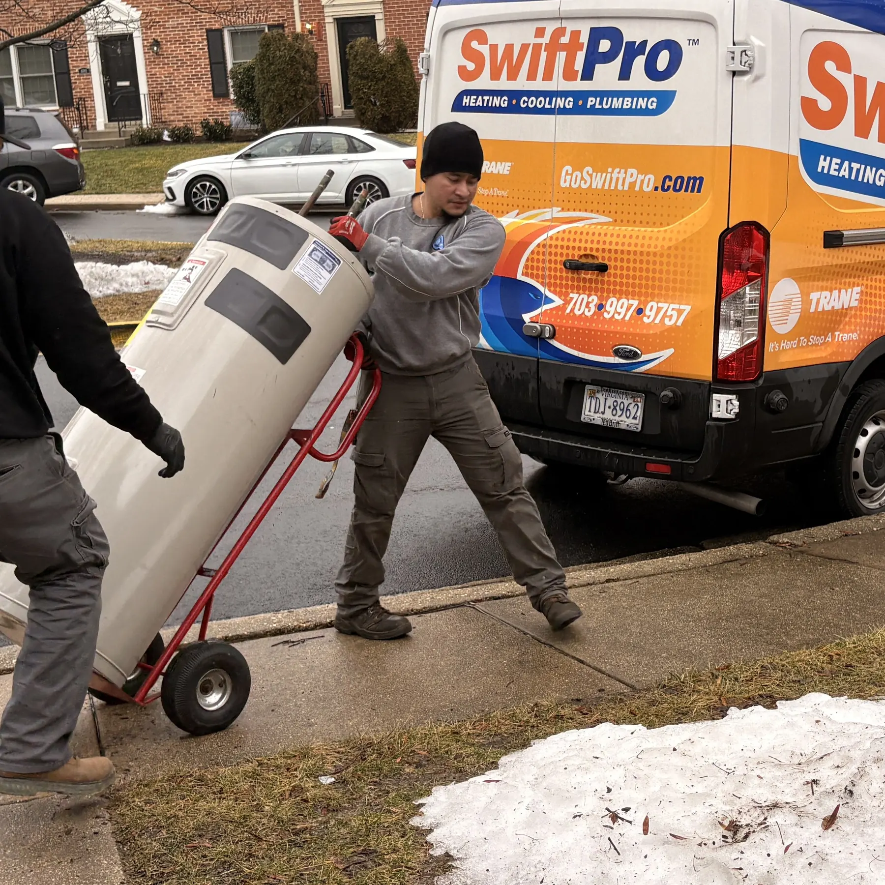 Two SwiftPro plumbers wheeling a new water heater past the van